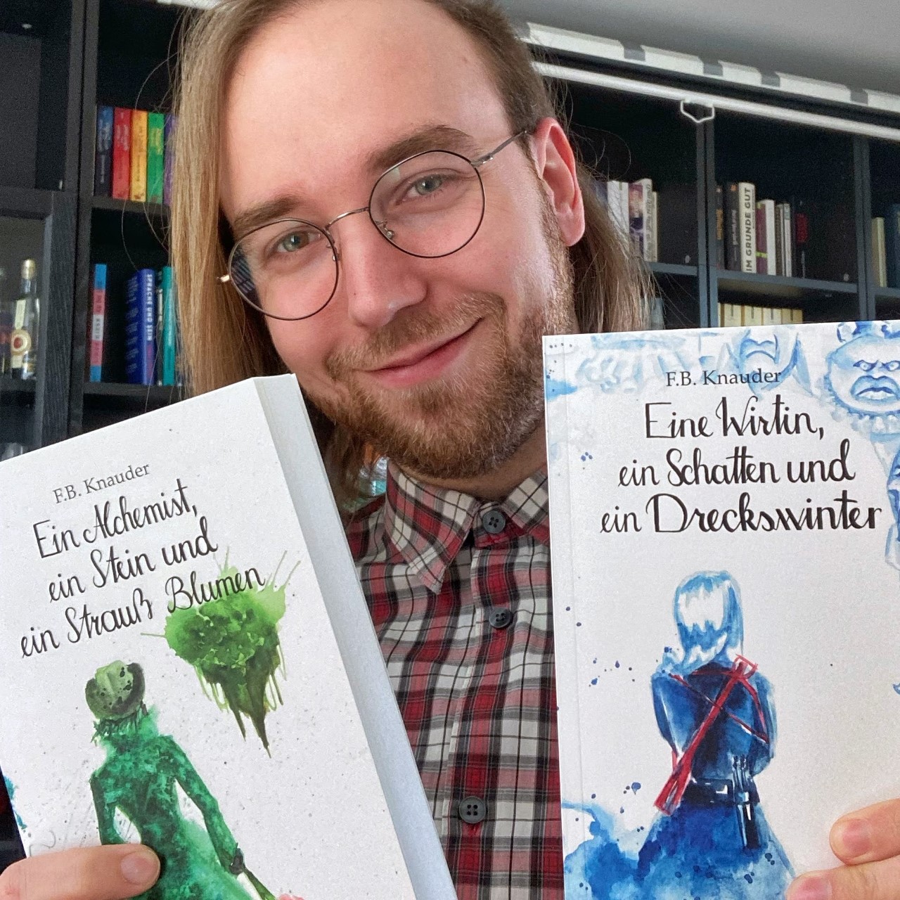 F.B. Knauder lächelt in die Kamera und hält zwei selbstgeschrieben Bücher hoch.